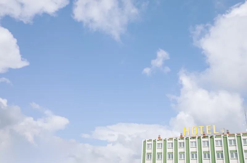 La esquina superior de un hotel asoma bajo un amplio cielo azul cubierto de nubes blancas.