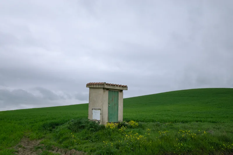 Pequeña construcción de hormigón aislada junto a un campo verde, bajo un cielo gris.