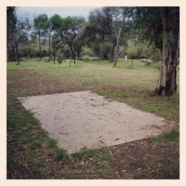 Losa rectangular de cemento, vacía y agrietada, en un claro arbolado.